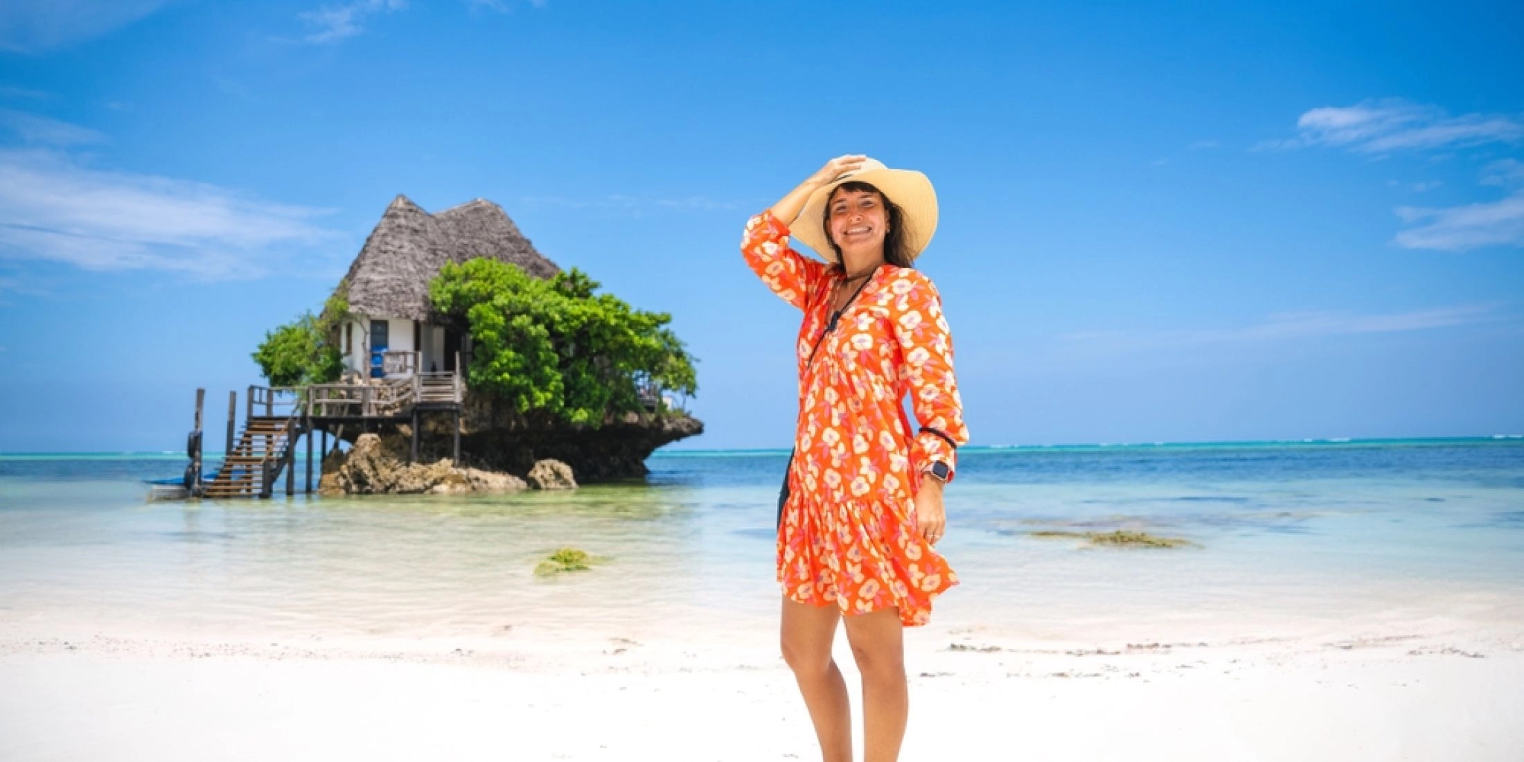 Kobieta w pomarańczowej sukience stoi na plaży przy restauracji The Rock na Zanzibarze.