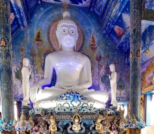 Wnętrze Wat Rong Suea Ten w Chiang Rai, biały posąg Buddy na tle niebieskich, bogato zdobionych malowideł, Tajlandia.