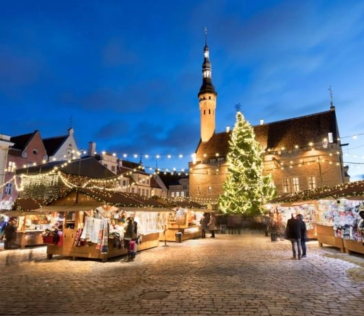 Jarmark świąteczny na Raekoja Plats w Tallinie, choinka i drewniane stragany na tle ratusza o niebieskim zmierzchu.