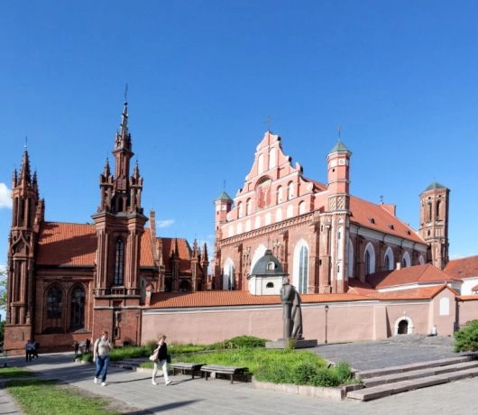 Kościoły św. Anny i Bernardynów w Wilnie współcześnie, z pomnikiem Adama Mickiewicza, ławkami i przechodniami na placu.