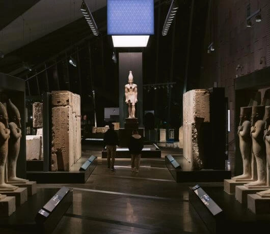 Wnętrze muzeum z szeregiem kamiennych posągów oświetlonych światłem ekspozycyjnym.