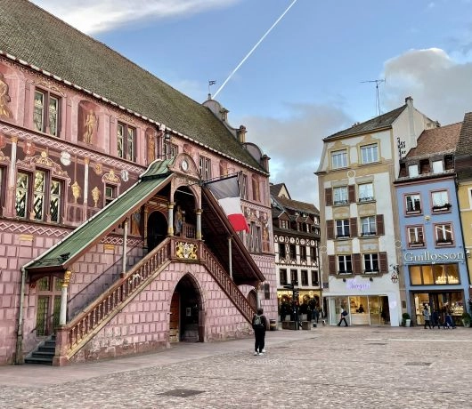 Ratusz w Miluzie na głównym placu miasta, zabytkowy budynek z malowaną fasadą i zewnętrznymi schodami w centrum historycznej starówki.