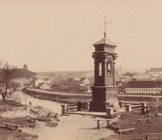 Kaplica Pana Jezusa na Śnipiszkach otoczona ławkami, z Wilią i panoramą dawnego Wilna w tle.