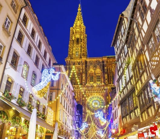 Ulica w Strasburgu z iluminacjami i widokiem na katedrę, bożonarodzeniowe dekoracje i stragany.