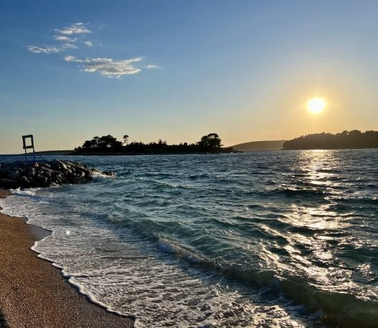 Zachód słońca nad Adriatykiem i fale rozbijające się o kamienistą plażę.