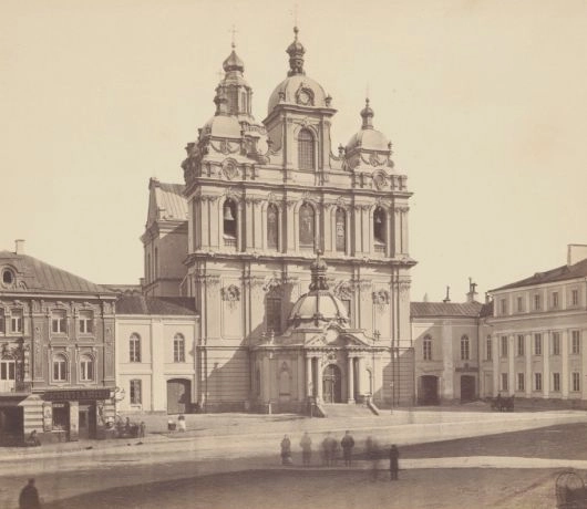 Kościół św. Kazimierza przy ulicy Wielkiej w Wilnie na archiwalnej fotografii, z cebulastymi hełmami i przechodniami przed fasadą.