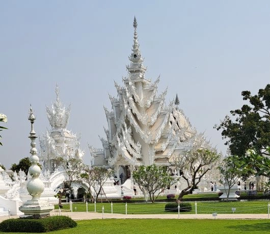 Wat Rong Khun w Chiang Rai, widok na Białą Świątynię otoczoną ogrodem i rzeźbionymi dekoracjami, Tajlandia.