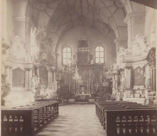 Wnętrze kościoła św. Michała w Wilnie na archiwalnej fotografii, z rzędami drewnianych ławek, bocznymi ołtarzami i ołtarzem głównym.