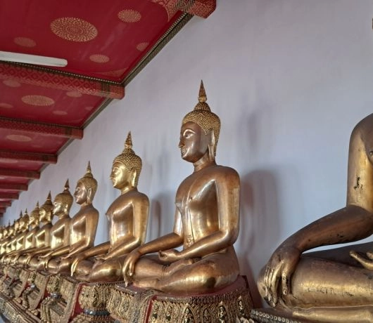 Rząd złotych posągów Buddy w Wat Pho w Bangkoku, ustawionych wzdłuż czerwonego sufitu świątyni.