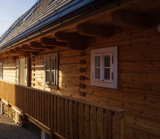 Drewniana chata z bali z długim zadaszonym gankiem, białymi oknami i drewnianą balustradą w Východnej na Słowacji.