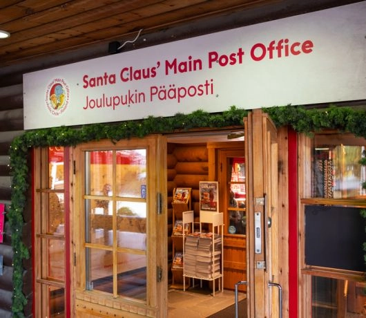 Wejście do głównej Poczty Świętego Mikołaja w Rovaniemi ozdobione zielonymi girlandami i drewnianymi drzwiami.