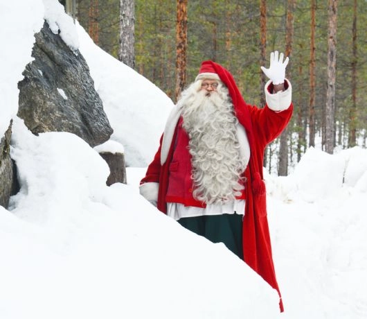 Święty Mikołaj w czerwonym płaszczu i z białą brodą pośród śniegu i lasu w Rovaniemi.