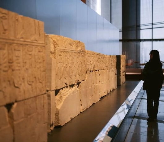 Osoba oglądająca starożytne płaskorzeźby z hieroglifami w oświetlonej galerii muzeum.