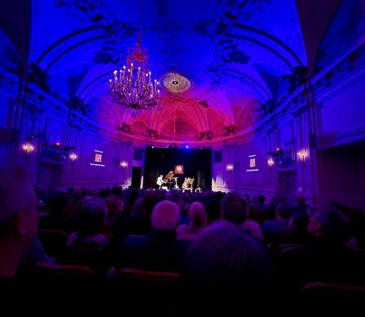 Muzycy grający na scenie w Salzburgu podczas festiwalu Jazz&TheCity, pianista, kontrabasista i perkusista w świetle reflektorów przed licznie zgromadzoną publicznością.