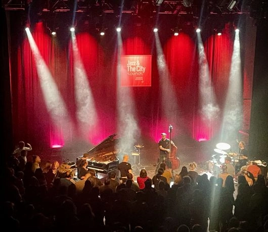 Publiczność w barokowej sali koncertowej w Salzburgu podczas wieczornego występu w ramach Jazz&TheCity, kolorowe światła oświetlają sklepienie i scenę.