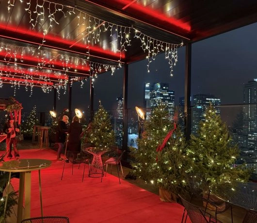 Świątecznie udekorowany taras widokowy z choinkami i panoramą Warszawy nocą.