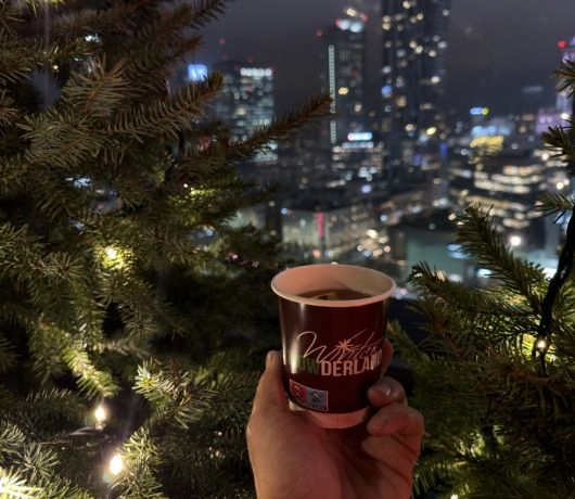 Świątecznie udekorowany taras widokowy z choinkami i panoramą Warszawy nocą.