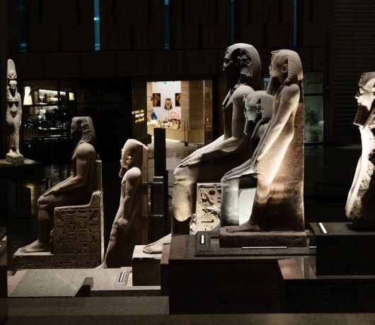 Grupa siedzących i stojących posągów oświetlonych punktowo w sali wystawowej GEM.