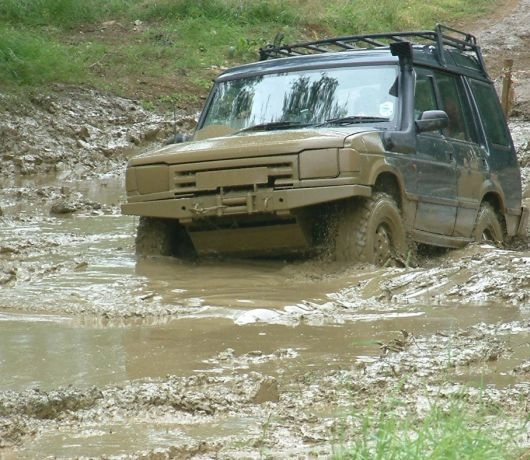 Samochód terenowy z napędem 4x4 pokonuje głębokie błoto i kałuże podczas wyprawy off-roadowej.