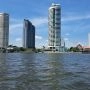 Panorama Bangkoku widziana z rzeki Chao Phraya, z nowoczesnymi wieżowcami i tradycyjnymi świątyniami w tle pod błękitnym niebem.