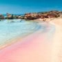Plaża Elafonisi na Krecie z jasną wodą, różowym piaskiem i niskimi skałami przy brzegu.