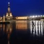 Plac sanktuarium w Fatimie nocą, z oświetloną bazyliką i postacią z parasolem odbijającą się w mokrej nawierzchni.