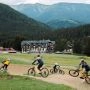 Grupa rowerzystów jedzie trasą w Donovalach na tle hoteli, lasów i górskich szczytów.