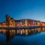 Wieczorna panorama nabrzeża Motławy w Gdańsku z Żurawiem, kolorowymi kamienicami i odbiciami świateł w wodzie.