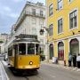 Żółty zabytkowy tramwaj numer 28 jedzie wąską ulicą Lizbony między kamienicami i kolorowymi fasadami.
