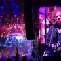 Koncert The Cure na festiwalu Pohoda, scena oświetlona czerwonym i niebieskim światłem, a na wielkim ekranie wokalista grający na gitarze.