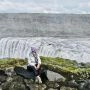 Autorka siedząca na skałach przy potężnym wodospadzie Dettifoss na Islandii.