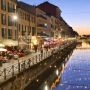 Dzielnica Navigli w Mediolanie po zmroku, z odbiciami świątecznych lampek w kanale i ogródkami restauracji.