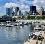 Port w Montrealu z zacumowanymi łodziami, spacerowym nabrzeżem i wieżowcami w tle.
