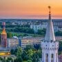 Panorama Opola o zachodzie słońca z miejskimi wieżami, zabudową centrum oraz osiedlami w tle.