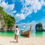 Kobieta na piaszczystej plaży obok tradycyjnej tajskiej łodzi, turkusowa woda i wapienne wyspy Phuket