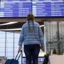 Podróżna z walizką spogląda na tablicę odlotów na lotnisku