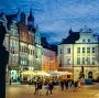 Stary Rynek w Poznaniu nocą z podświetlonymi kamienicami i spacerującymi ludźmi.