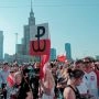 Tłum uczestników obchodów Powstania Warszawskiego z biało-czerwonymi flagami i znakiem Polski Walczącej w centrum Warszawy.