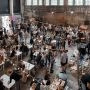 Tłum ludzi przy stolikach i stoiskach gastronomicznych w industrialnym wnętrzu dawnej fabryki
