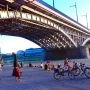Praski brzeg Wisły w Warszawie pod mostem Poniatowskiego z rowerami, plażą i odpoczywającymi ludźmi.