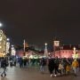 Świąteczny Plac Zamkowy w Warszawie nocą: choinka, iluminacje i spacerujący ludzie na starówce zimą.