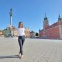 Kobieta stojąca na placu Zamkowym w Warszawie, w tle kolumna Zygmunta i Zamek Królewski.