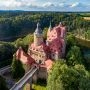 Lotnicze ujęcie Zamku Czocha od strony wieży i jeziora, otoczonego gęstym lasem.
