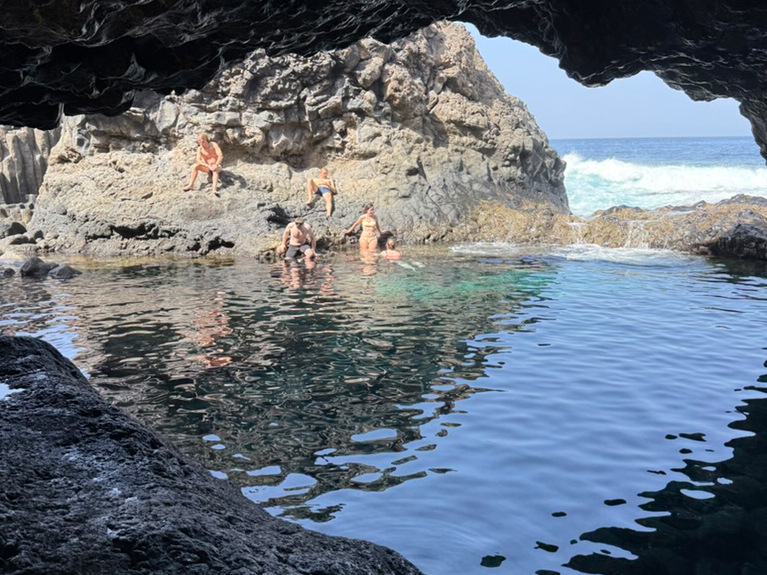 Naturalny basen lawowy na El Hierro z osobami kąpiącymi się w ciemnej skalnej grocie nad oceanem.