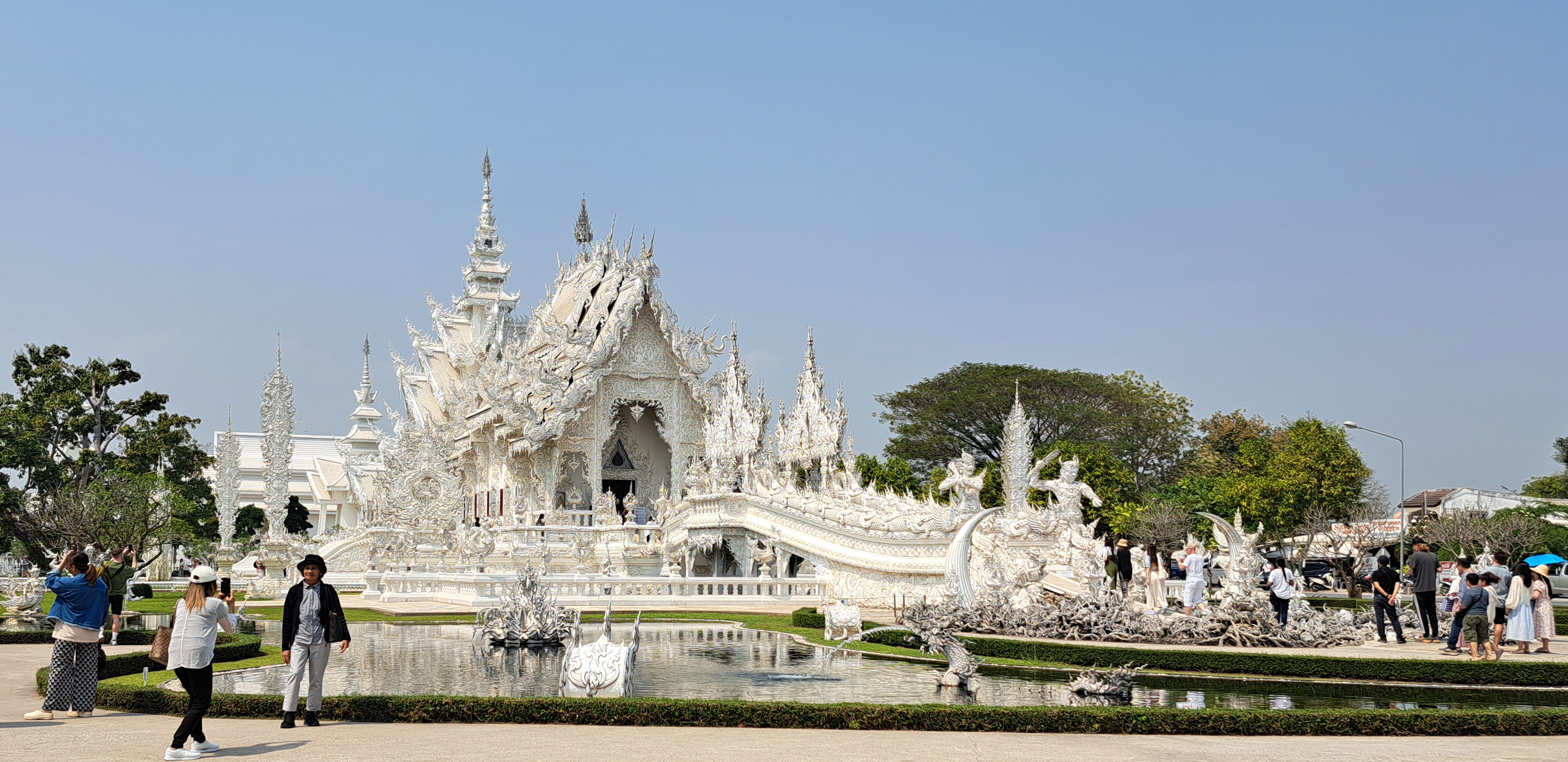 Wat Rong Khun w Chiang Rai, Biała Świątynia z rzeźbioną fasadą i mostem nad stawem, Tajlandia.