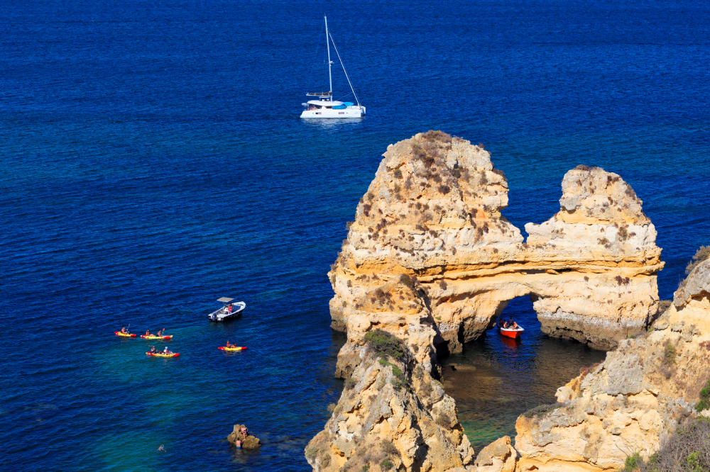Formacje skalne Ponta da Piedade na wybrzeżu Algarve, kajaki i jacht na Atlantyku, błękitne morze, statek w tle