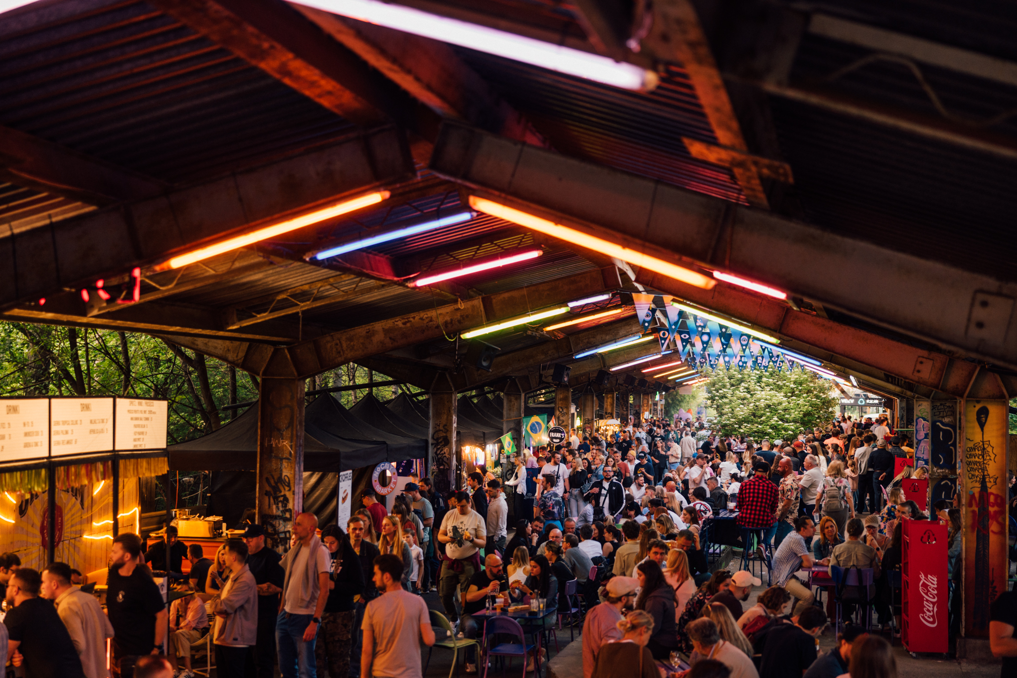 Wieczorny widok na Nocny Market z tłumem gości, kolorowymi neonami i stoiskami gastronomicznymi pod zadaszeniem dawnych peronów.