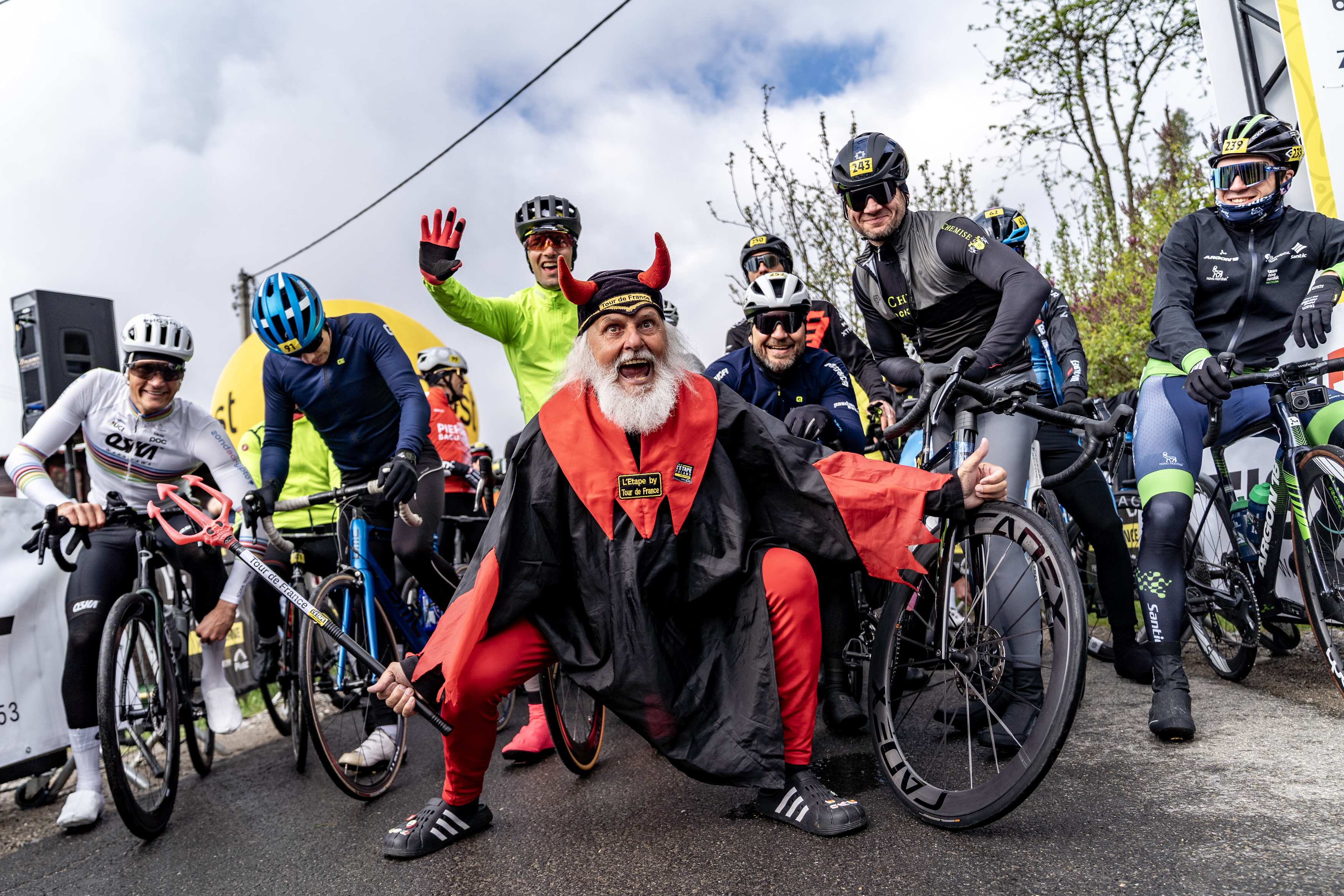 Kolarze stoją na starcie wydarzenia L’Étape Poland by Tour de France, obok nich maskotka Tour de France pozuje do zdjęcia.