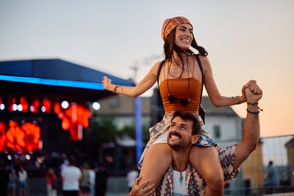 Uśmiechnięta para bawi się podczas letniego festiwalu plenerowego przy scenie koncertowej.