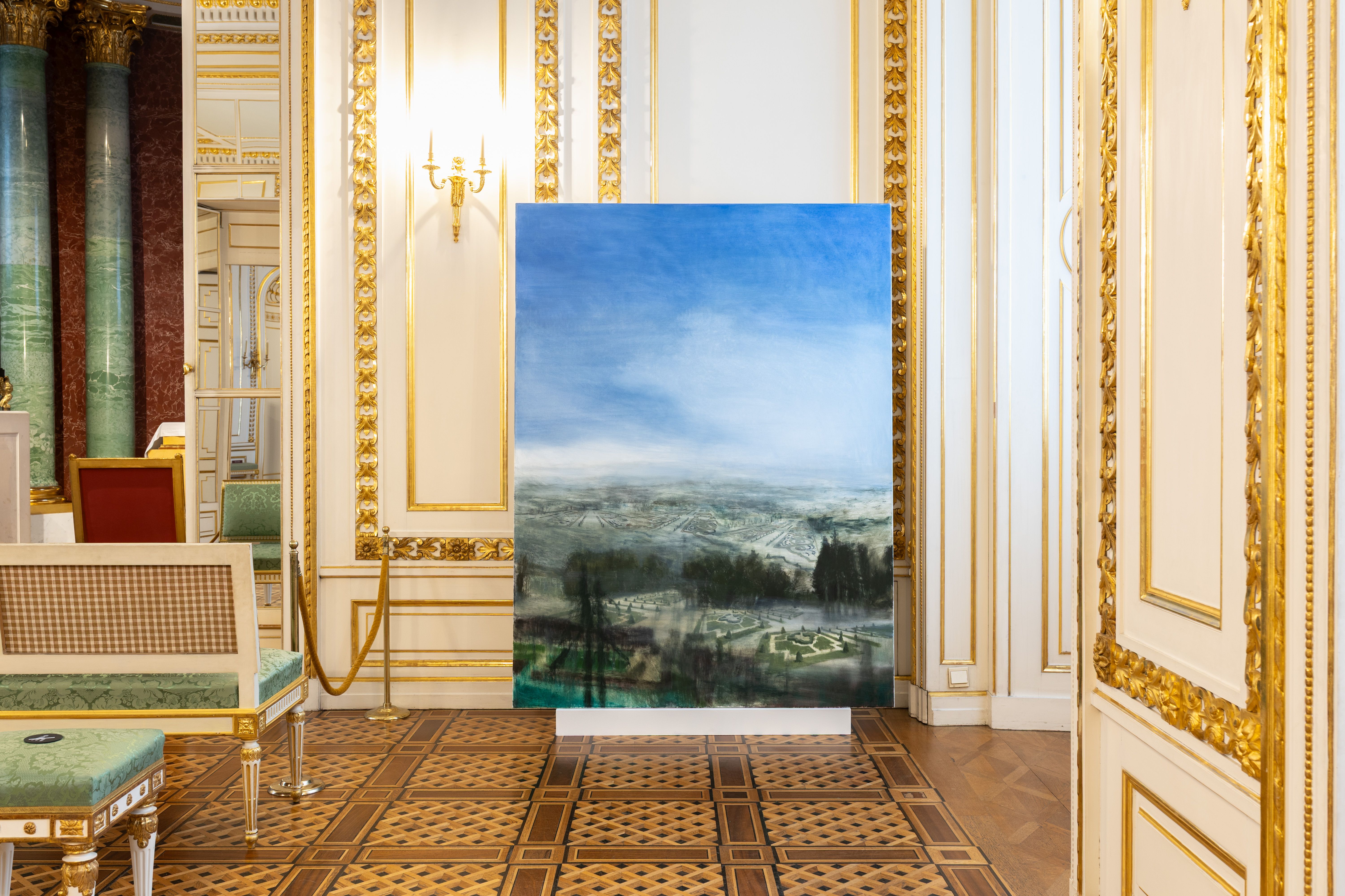 Obraz Łukasza Stokłosy przedstawiający rozległy krajobraz ustawiony w złoconej sali Zamku Królewskiego w Warszawie, z klasycznymi kolumnami, dekoracyjnymi ścianami i parkietem.